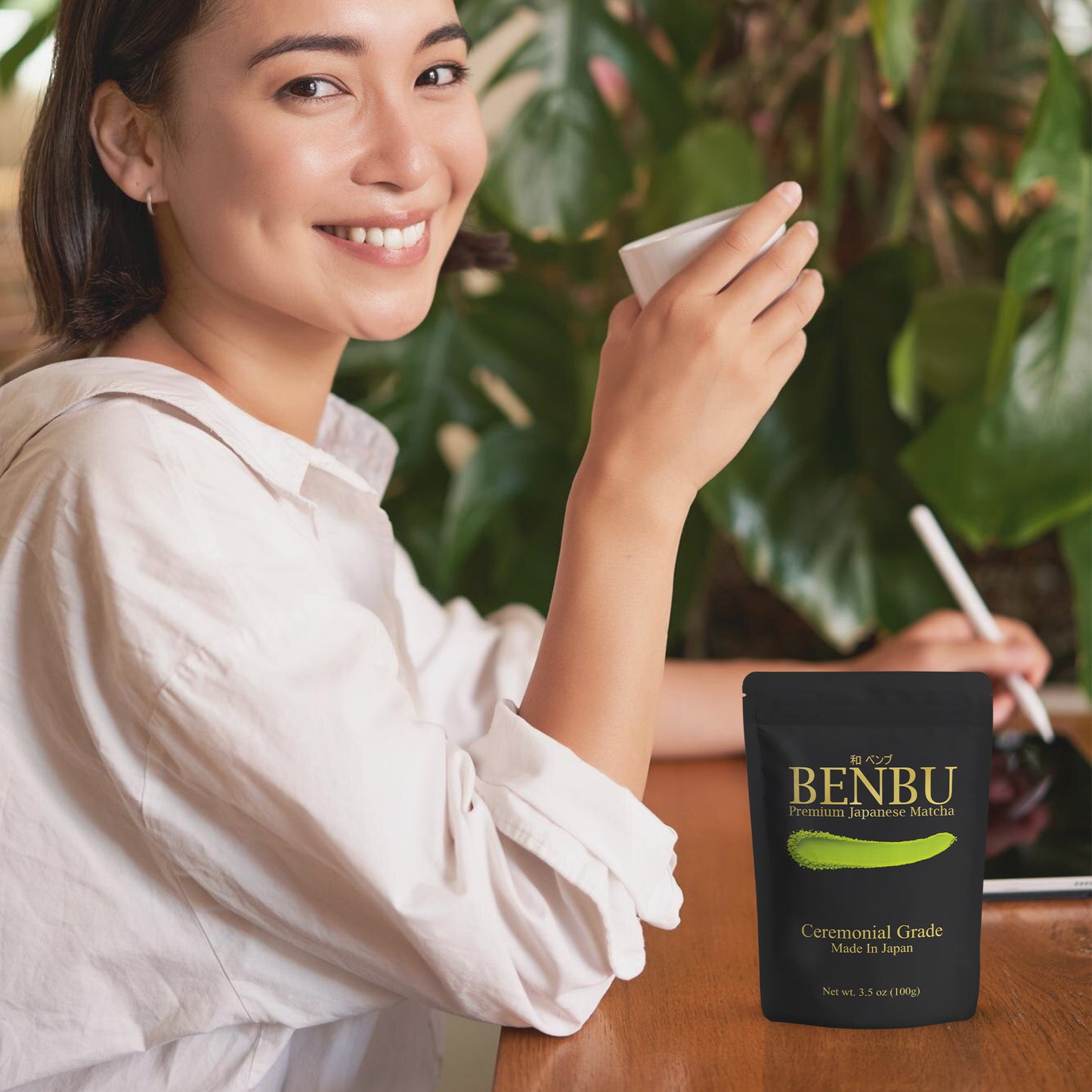 Woman drinking BENBU Matcha with 100 g bag on wooden table