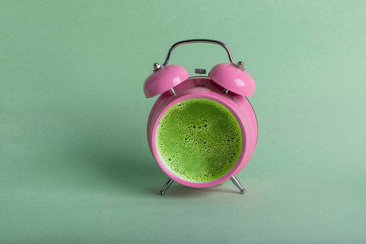 Tasty matcha tea in a pink retro alarm clock on green background. Waking up with alarm and green tea concept