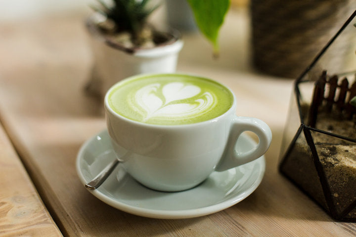 Green tea matcha latte art with succulent cropped at an angle at a coffee shop cafe on wooden table