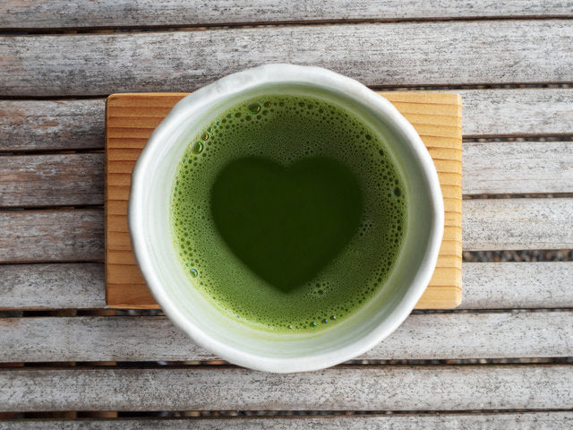 Top view of organic green tea matcha with heart shape in foam in white japanese style ceramic bowl after ceremony processing