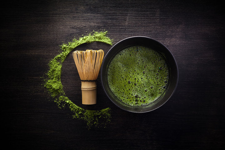Overhead of bright green matcha fine froth in a ceramic bowl with a whisk next to it.