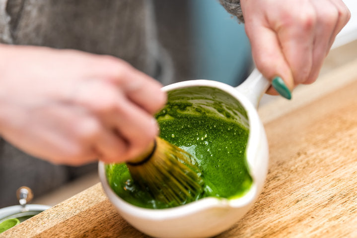 Woman holding Japanese tea cup teapot pot on table closeup holding whisk for matcha stirring hot drink koicha