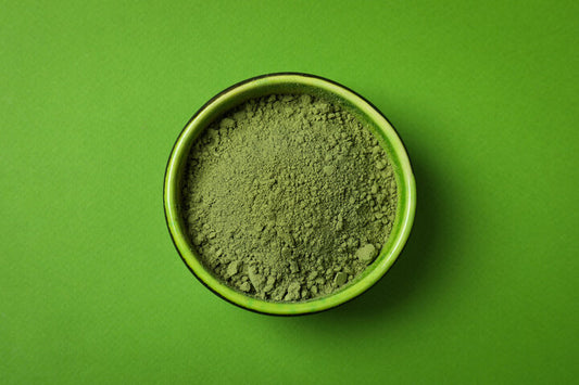 Green bowl of matcha powder on matching green background