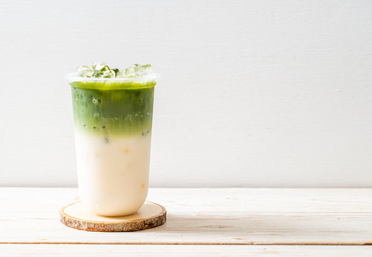 Layered iced matcha latte in glass on wooden coaster