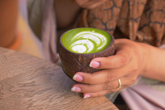 Hands holding a dark cup with green matcha latte and white latte art — Does Matcha Have Caffeine?