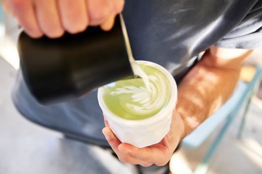 Milk being poured into green latte in white cup — How to Make Matcha
