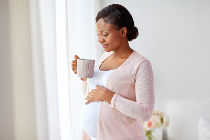 Pregnant woman holding mug indoors near window