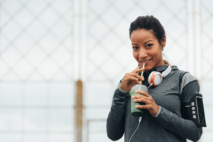 Athletic woman drinking green smoothie with headphones