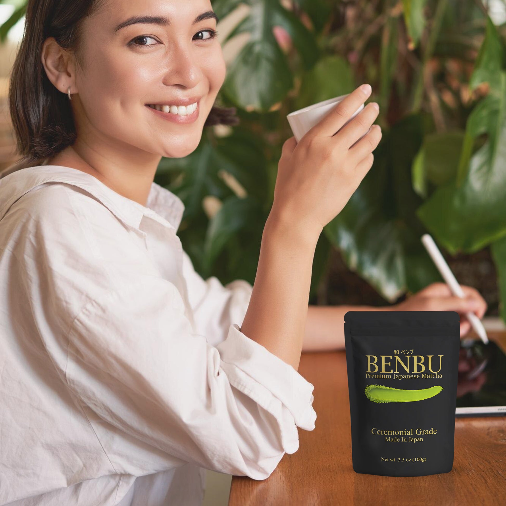 Woman drinking BENBU Matcha with 100 g bag on wooden table